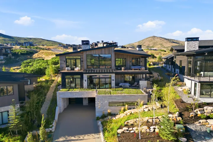 Modern architectural design featuring expansive glass windows, multiple balconies, a flat roofline, and a stone and wood-paneled exterior