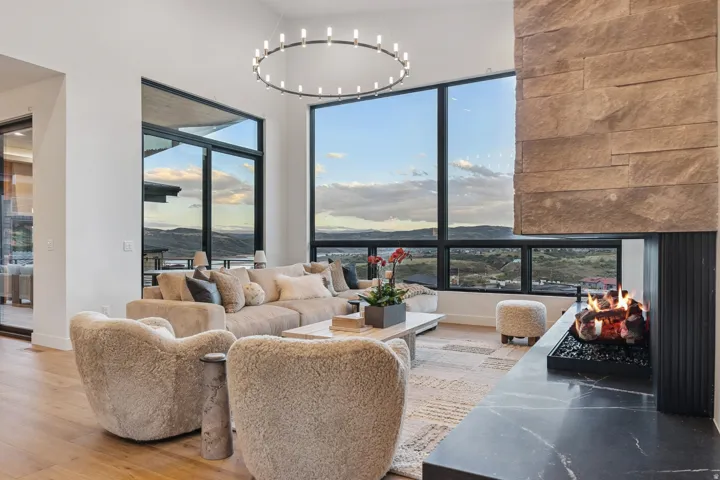 High ceilings with a circular chandelier, expansive windows with dark framing, wood-finish flooring, a stone-clad fireplace, and a dark stone hearth
