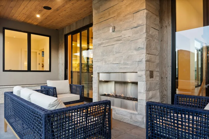 Outdoor living area featuring a stacked stone fireplace with a built-in fire feature, a wood-paneled ceiling, recessed lighting, and large glass sliding doors