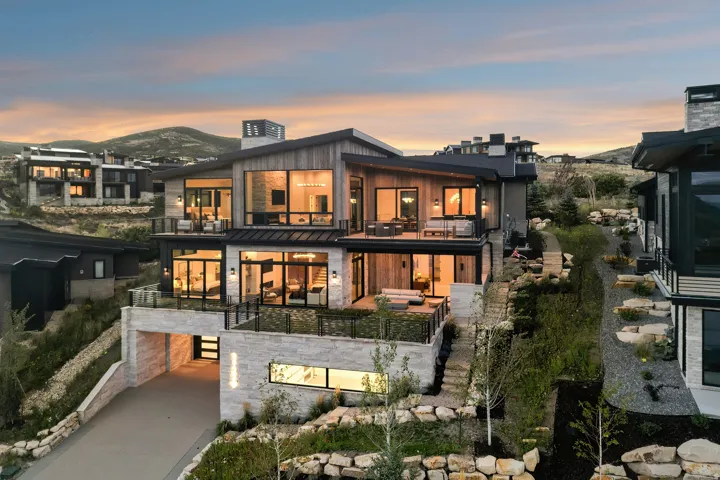 Modern architectural design with multiple balconies, extensive window placements, a stone and wood facade, and a built-in garage