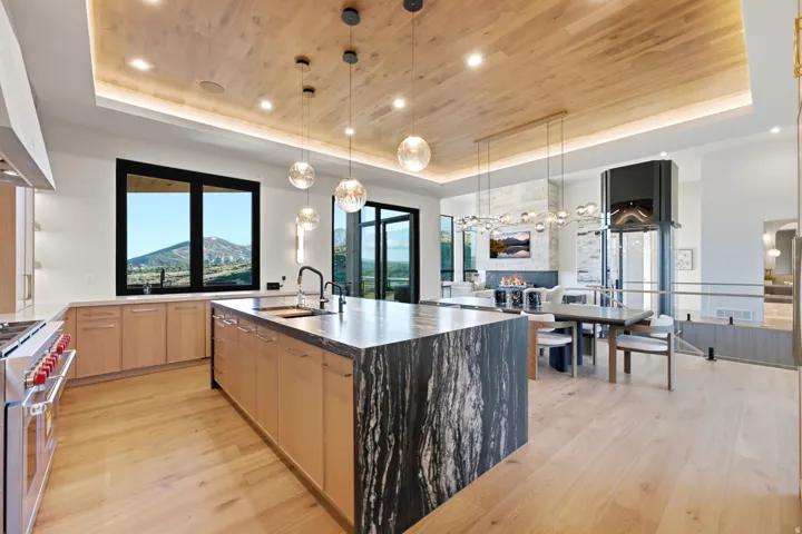 Kitchen featuring wood-finish flooring, natural wood cabinetry, a large kitchen island with a stone countertop, modern pendant lighting, and a built-in oven