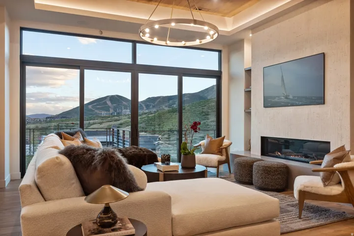 Floor-to-ceiling windows, linear fireplace with media display, tray ceiling with recessed lighting, wood-finish flooring, and a large private balcony