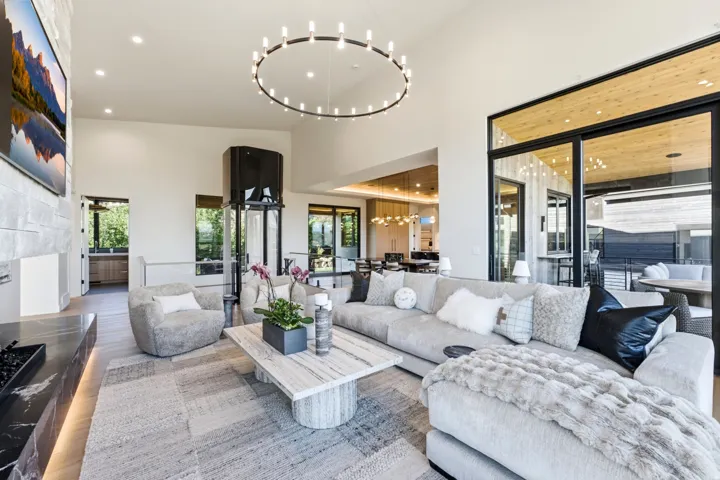 Spacious living area featuring a vaulted ceiling with a circular chandelier, a stone-clad fireplace, and expansive sliding glass doors