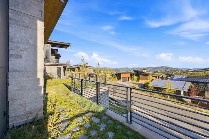 Stone facade with an expansive outdoor walkway featuring a modern metal railing, integrated landscaping, and distant mountain scenery