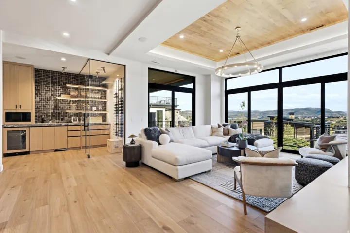 Wood-finish flooring, built-in wet bar with beverage cooler, full-height glass wine storage, wood-paneled ceiling with recessed lighting, and expansive windows