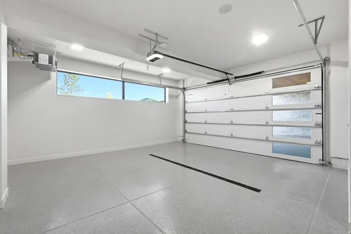 White garage door with rectangular window inserts, light gray epoxy flooring, recessed ceiling lighting, and a high-set horizontal window