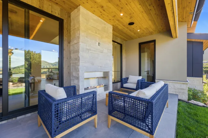 Outdoor patio featuring a stone-clad fireplace, wood-plank ceiling with recessed lighting, and large sliding glass doors