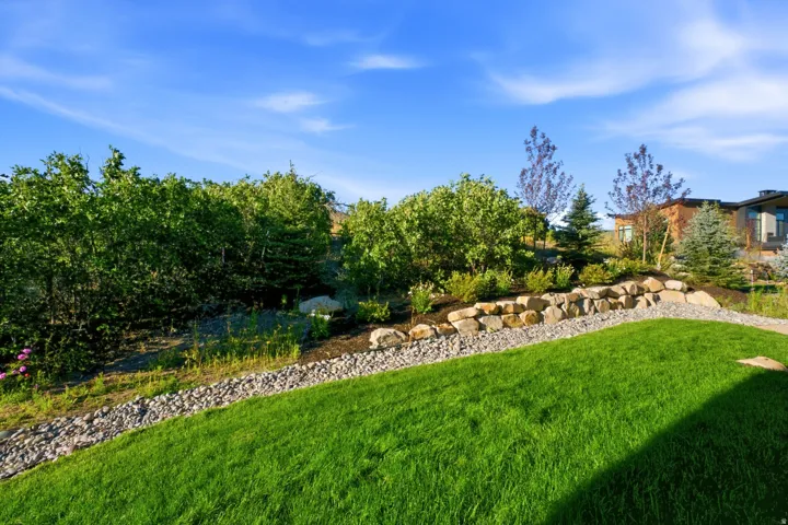 Manicured lawn, rock retaining wall, mature landscaping, gravel pathway, and distant building structure