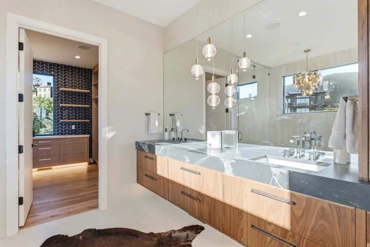 Dual vanity with stone countertops and integrated sinks, wood-finish cabinetry, full-wall mirror, and pendant lighting