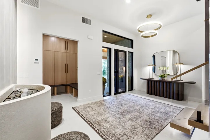 Modern entryway featuring a built-in wood-finish storage system, a suspended double-ring chandelier, and a floating staircase with a glass panel