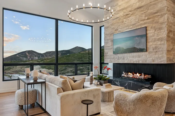 Floor-to-ceiling windows, stone-clad fireplace with gas logs, black marble hearth, circular chandelier, and wood-finish flooring