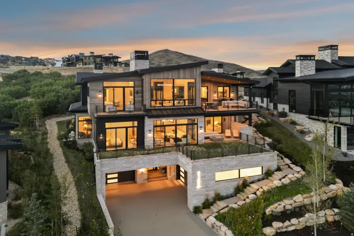 Multi-level exterior featuring extensive glass, multiple balconies, a lower-level drive-under garage, stone cladding, and a flat roofline
