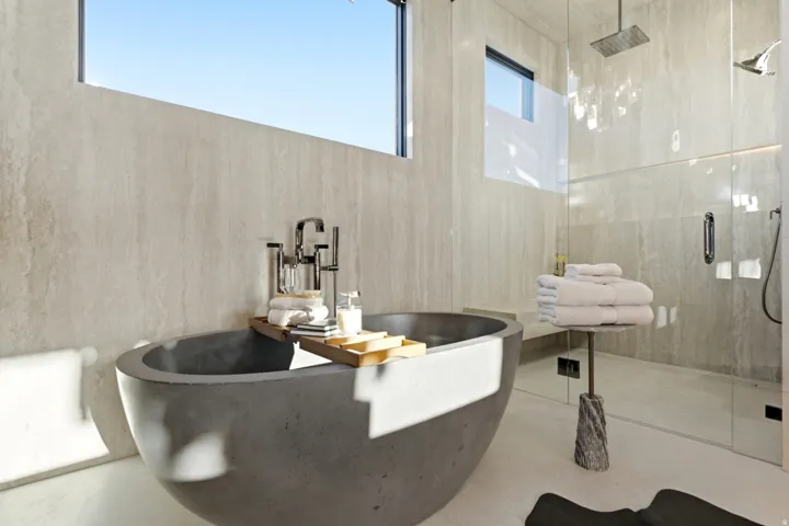Freestanding soaking tub with floor-mounted faucet, glass-enclosed shower with rain head and wall-mounted shower head, and light-toned wall tiling
