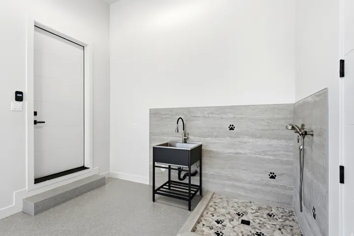 Dedicated pet washing station featuring a wall-mounted shower head, pebble tile flooring, a black basin sink with a gooseneck faucet, and surrounding stone-finish wall tile