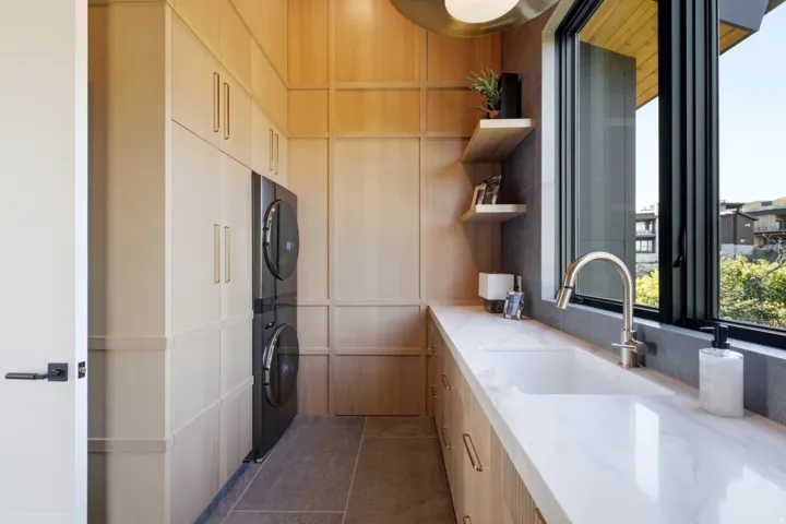 Integrated washer and dryer, extensive built-in cabinetry, solid surface countertop with integrated sink, modern faucet, and large casement window