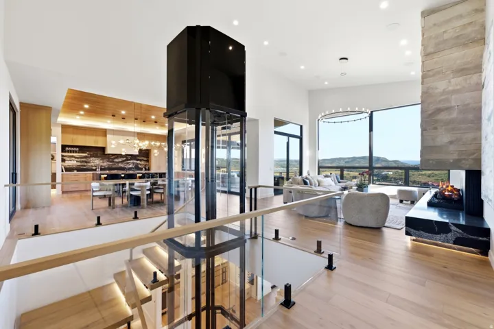 Glass-enclosed elevator, wood-finish flooring, stone-clad fireplace, floor-to-ceiling windows, and recessed lighting