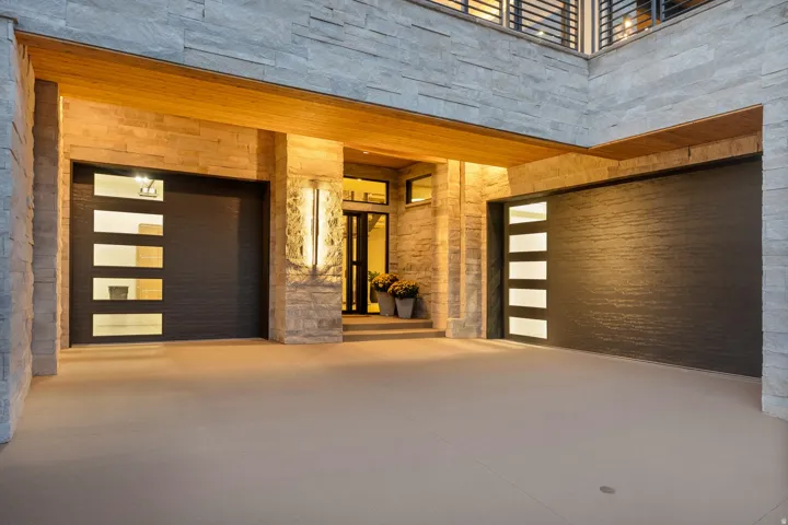 Stacked stone exterior, dual garage doors with frosted glass panels, wood-finish soffit, and an illuminated entryway