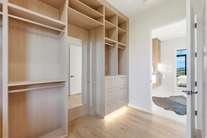 Built-in cabinetry with extensive shelving and hanging rods, integrated drawers with metal hardware, recessed under-cabinet lighting, and wood-finish flooring