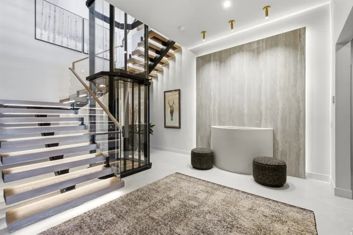Floating staircase with glass railing, integrated lighting, and a private elevator