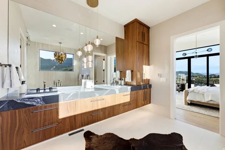 Dual vanity with stone countertops, wood-finish cabinetry, and contemporary pendant lighting