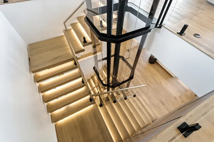 Light wood-finish flooring, glass panel railings, and a central glass elevator