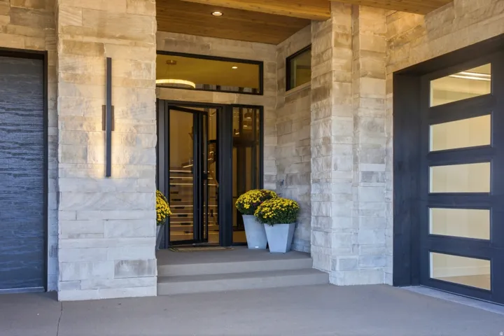 Stacked stone facade with a wood-clad soffit, contemporary sconce lighting, and a multi-pane entry door