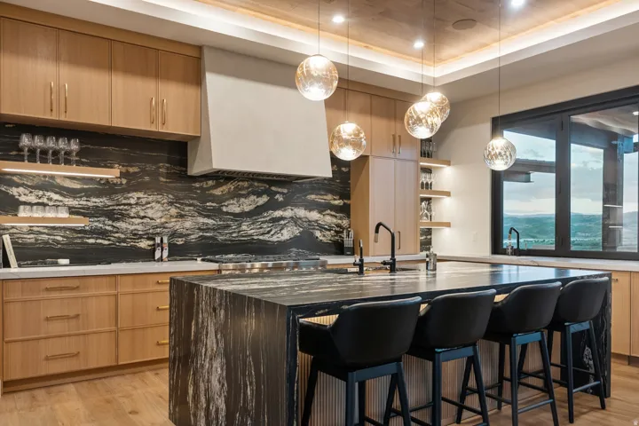 Gourmet kitchen featuring a waterfall island, professional-grade range, custom light wood cabinetry, and a striking natural stone backsplash