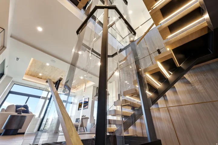 Two-story glass elevator, illuminated open-tread staircase, glass railings, and expansive windows