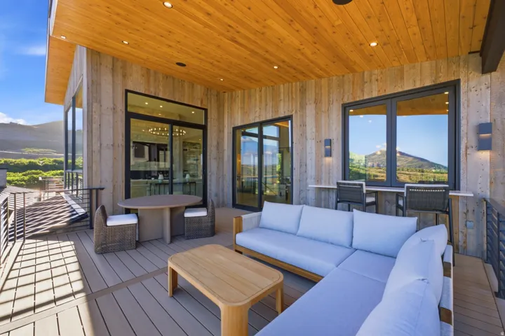 Expansive outdoor living area featuring a wood-plank ceiling with recessed lighting, composite decking, and a metal railing