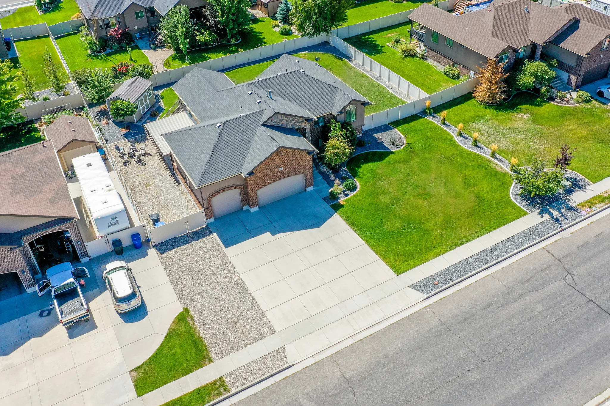 Expansive concrete driveway, attached two-car garage, mature landscaping, and an additional gravel parking area