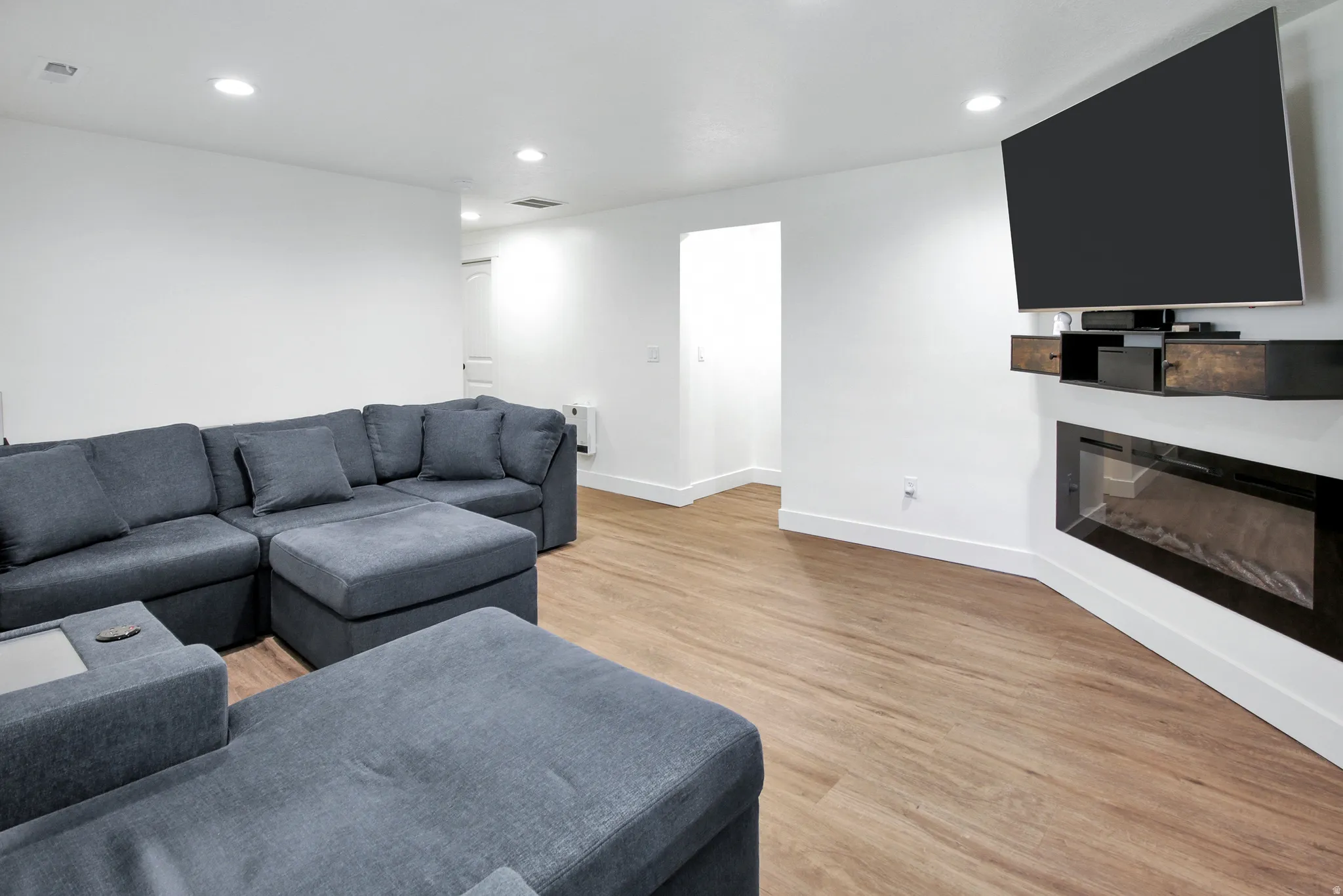 Wood-finish flooring throughout, recessed ceiling lighting, wall-mounted electric fireplace, and white baseboards