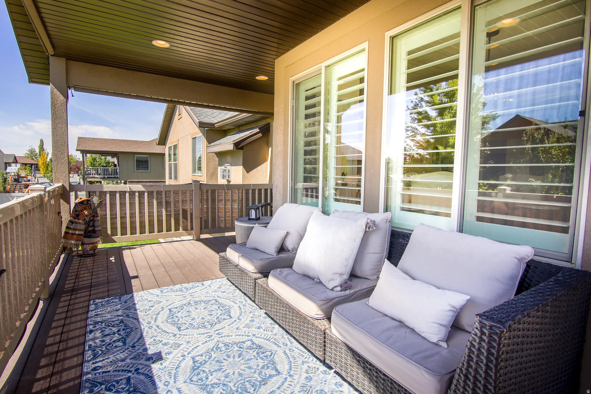 Covered outdoor patio with a composite deck surface, white sliding glass doors, and white interior plantation shutters
