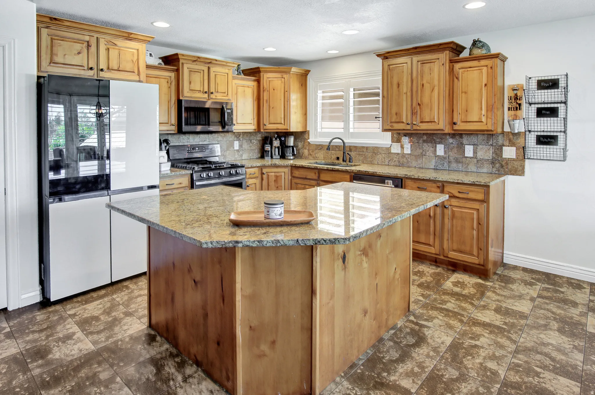 Kitchen featuring wood cabinetry, granite countertops, tile backsplash, and a central island with countertop seating