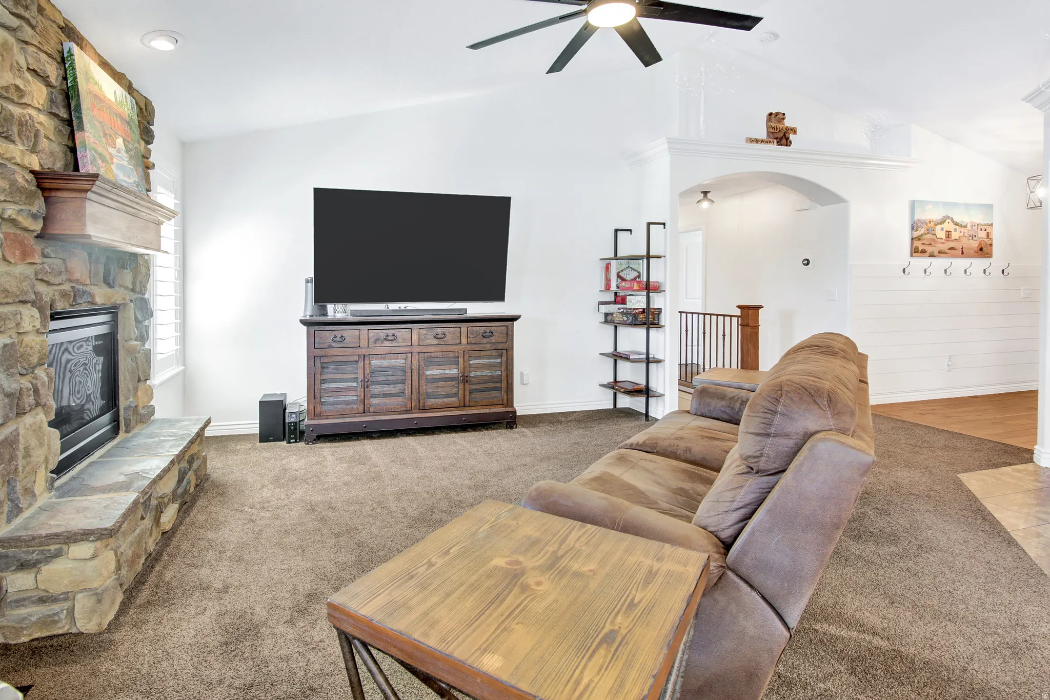 Vaulted ceilings, stone-clad fireplace with mantel, ceiling fan, and carpeted flooring