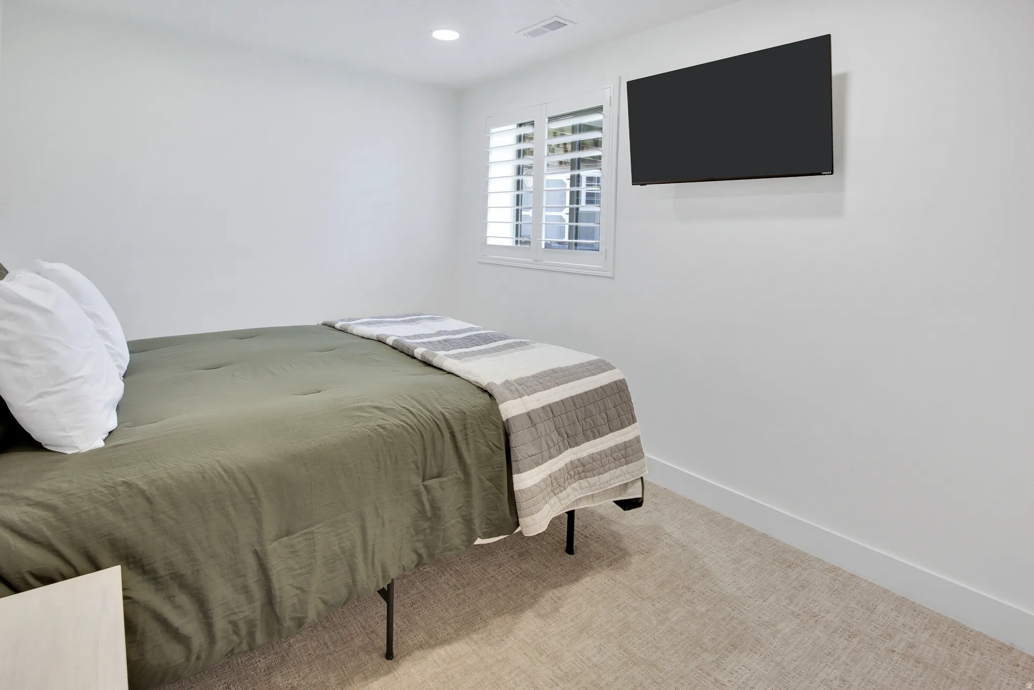 Recessed lighting, wall-mounted television, window with plantation shutters, light-toned carpeting, and white walls
