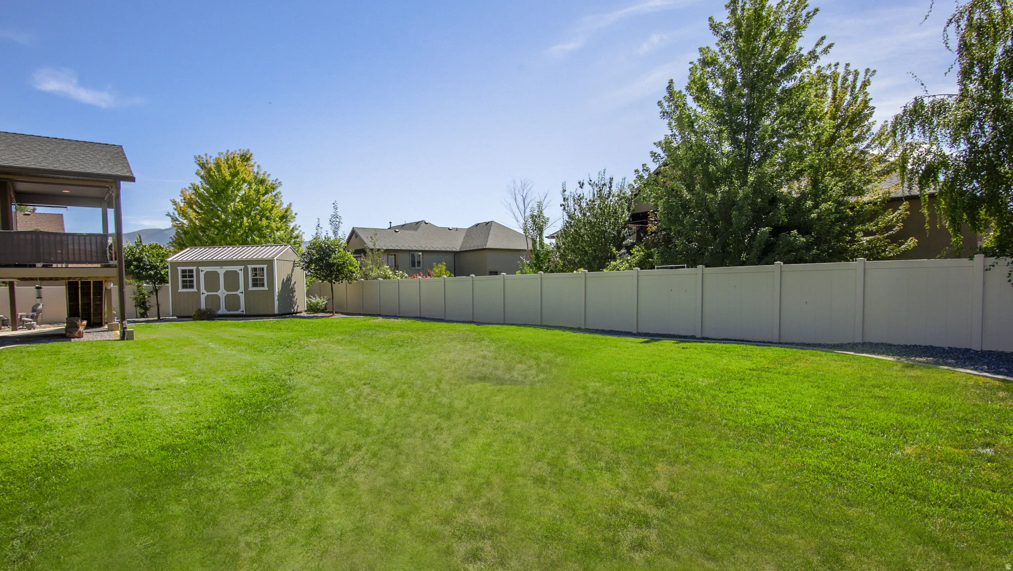 Expansive green lawn with a privacy fence, a detached storage shed, and mature trees