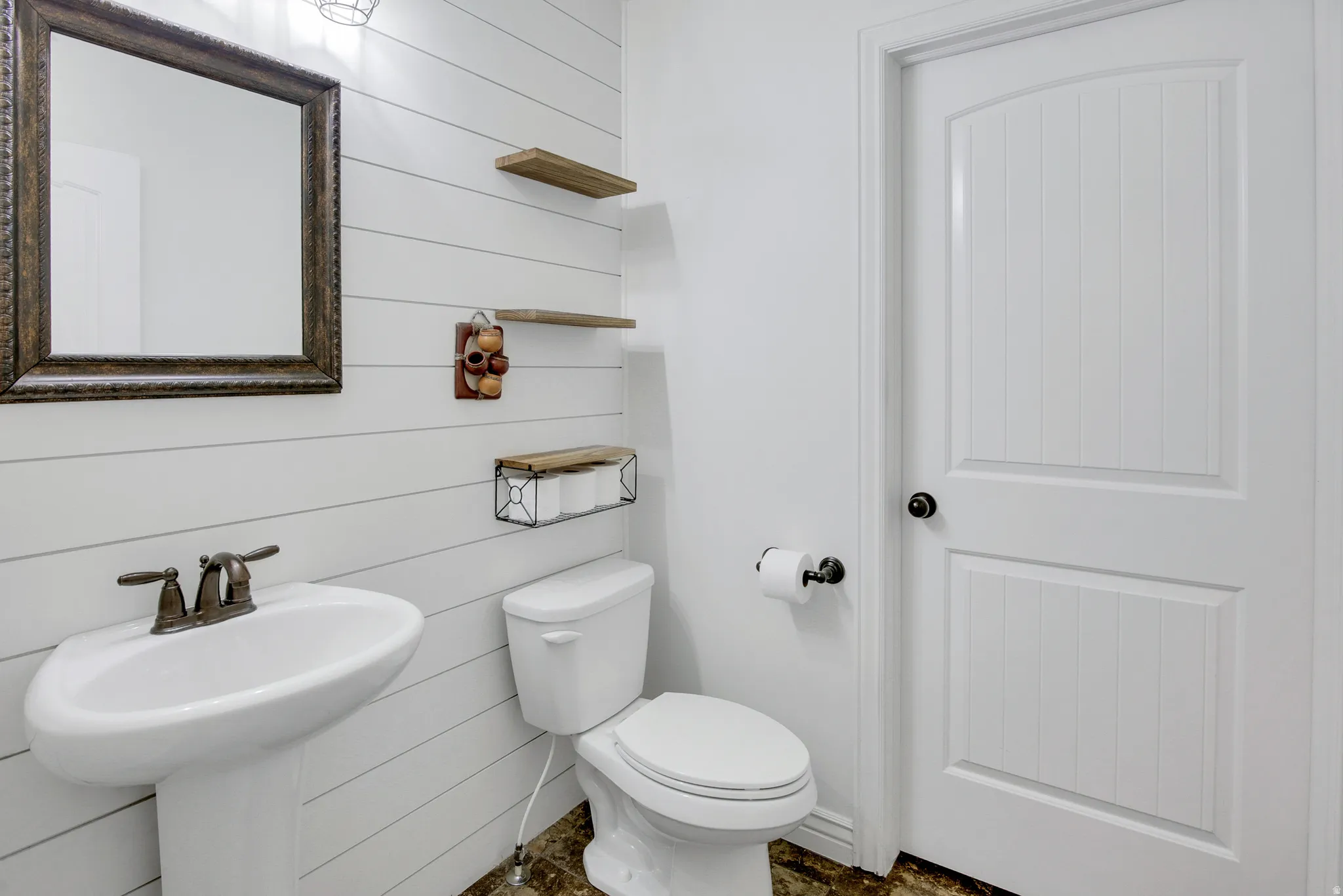 Pedestal sink with bronze-finish faucet, framed wall mirror, shiplap wall paneling, and a panel-style door