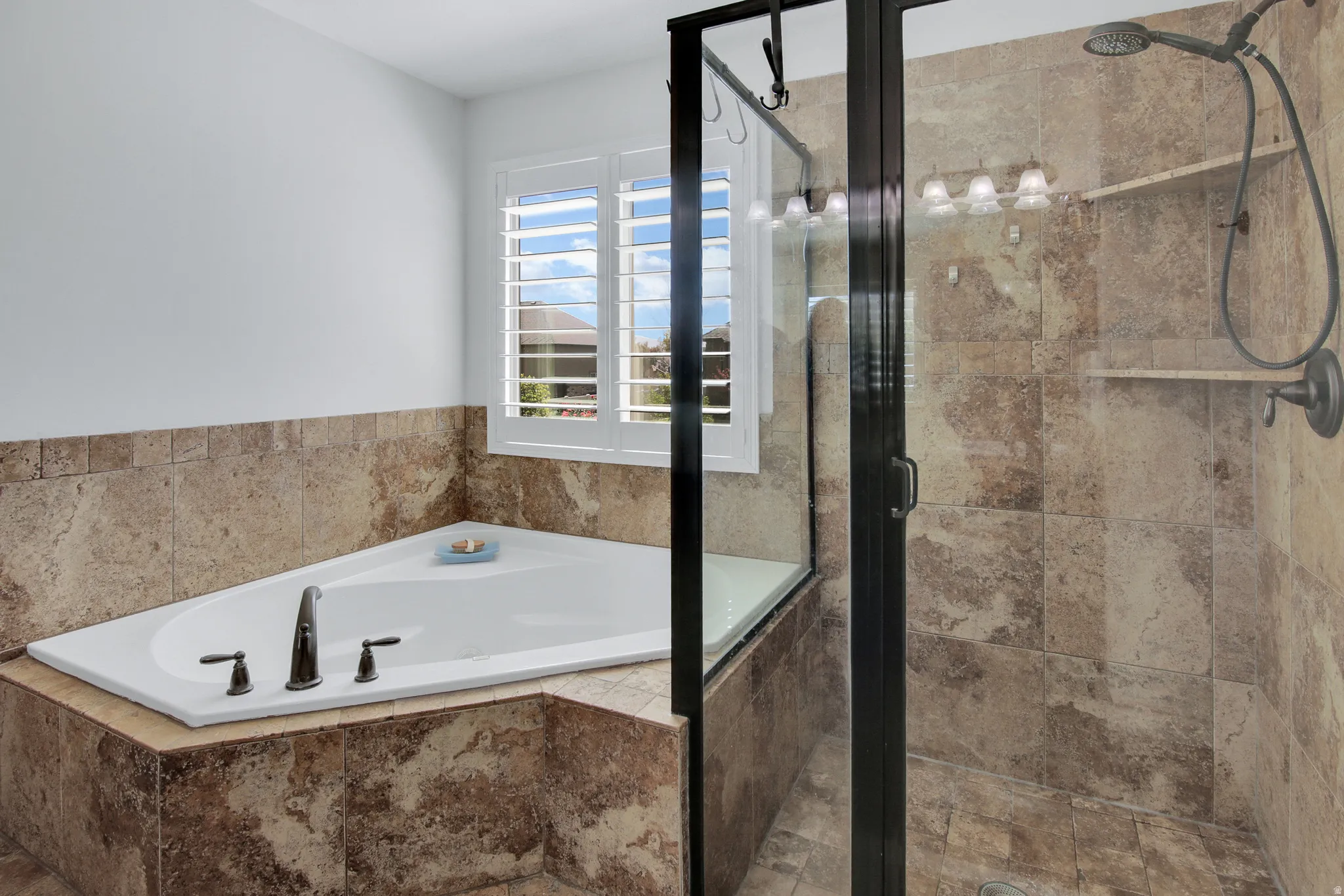 Corner soaking tub with bronze-finish fixtures, tile surround, and plantation shutters