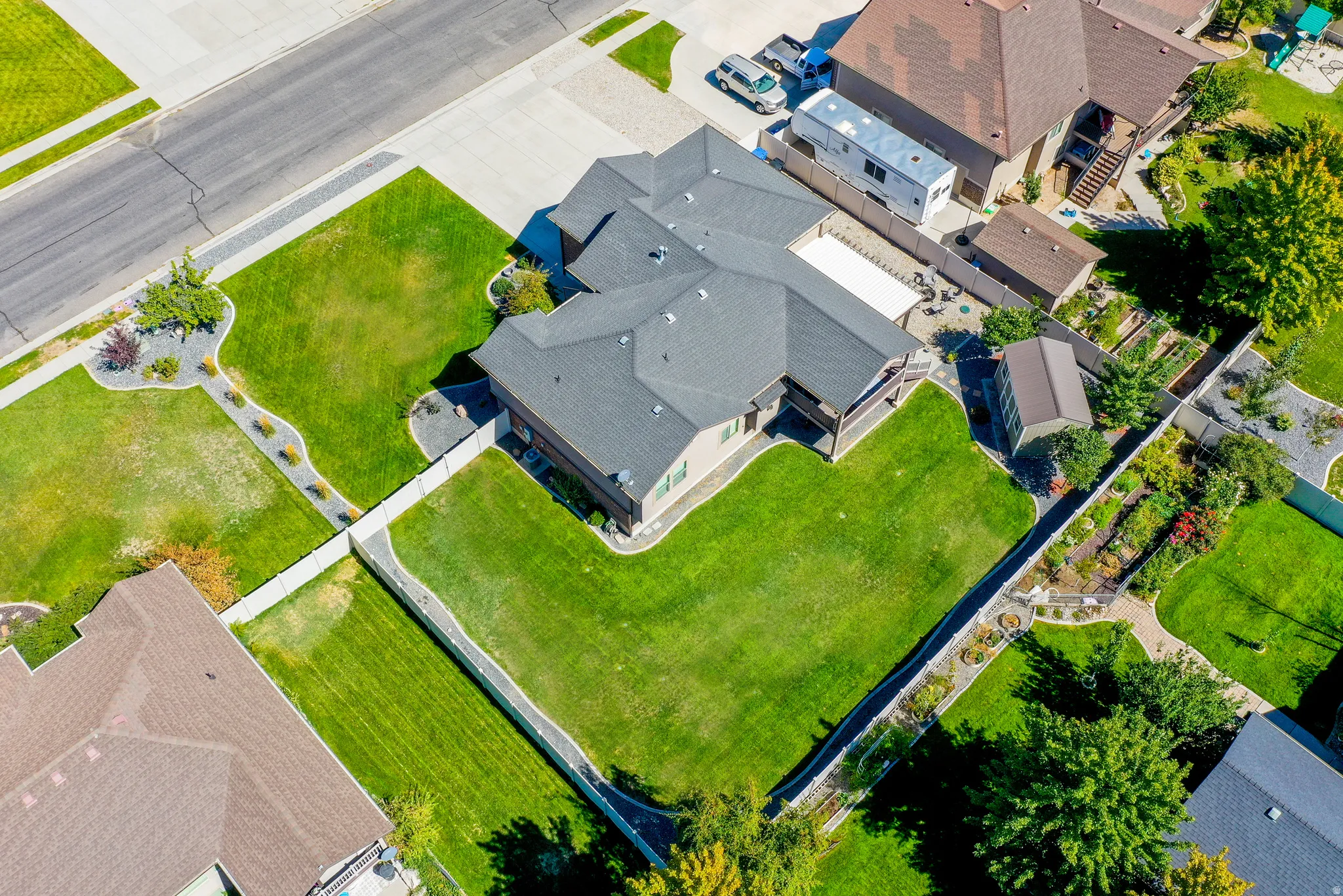 Expansive green lawn surrounds the property, featuring a multi-level structure with a dark shingled roof, an outdoor patio, and a detached shed