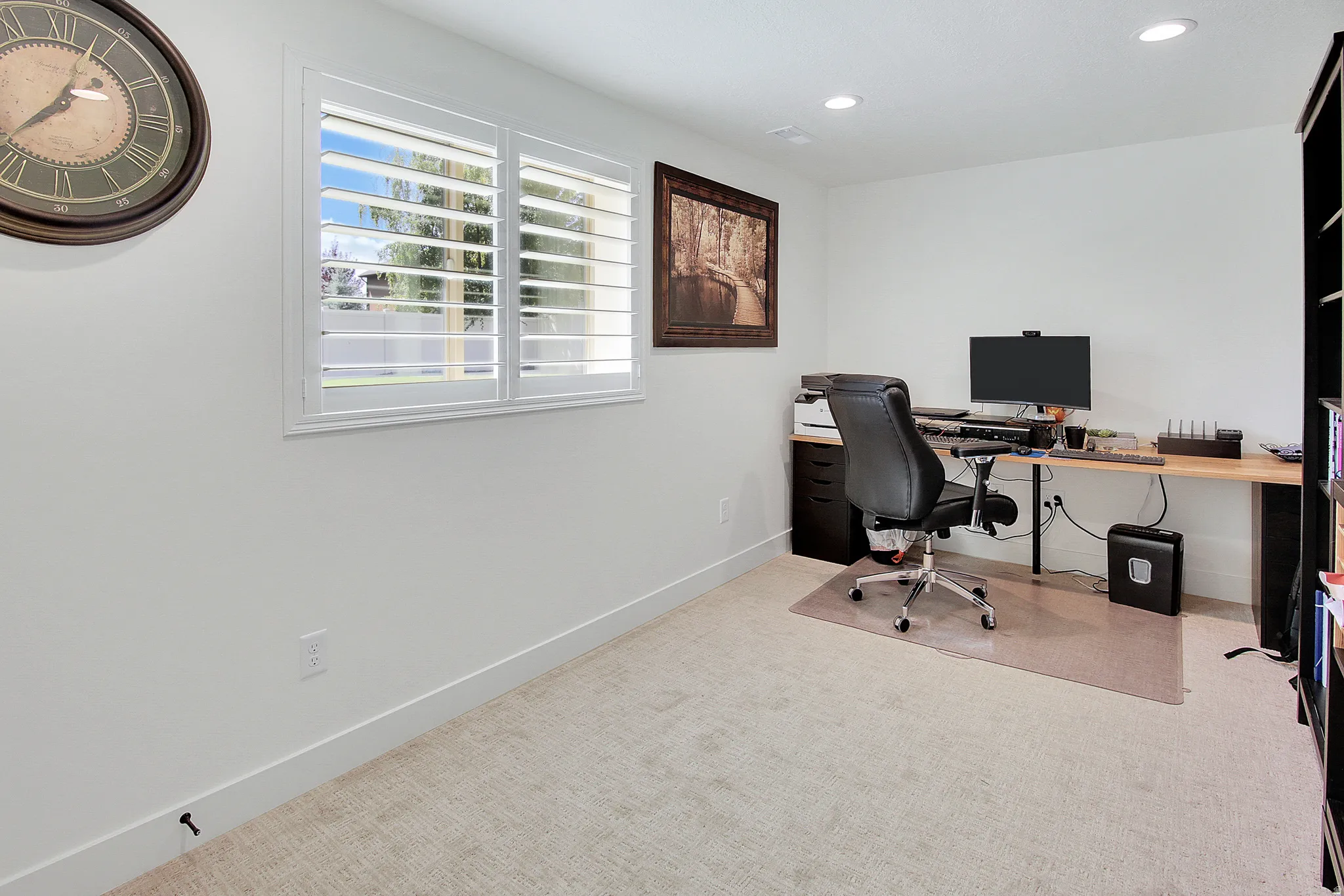Recessed lighting illuminates the room, featuring a window with plantation shutters and carpeting