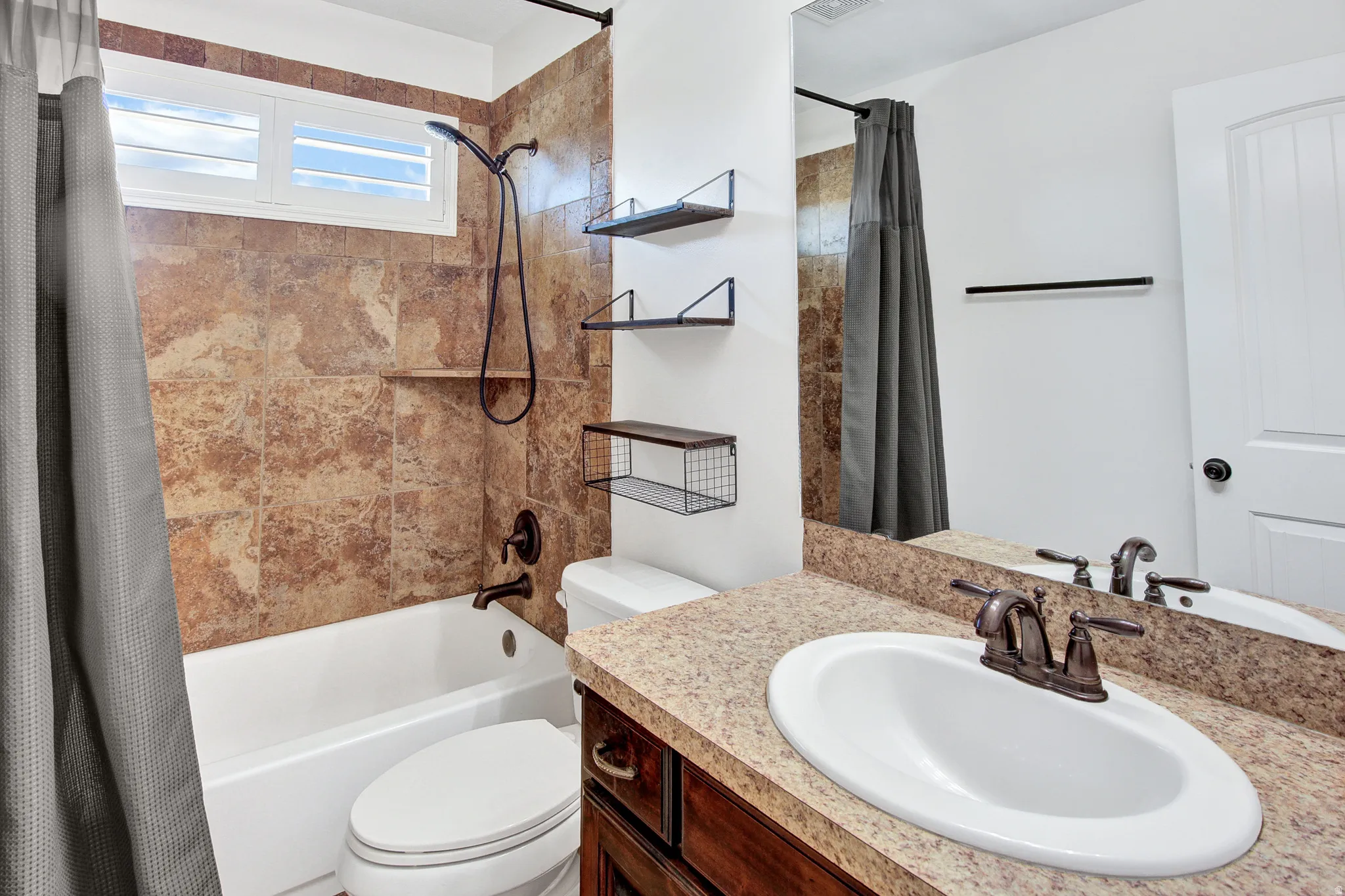 Built-in bathtub with a shower head, stone-finish wall tile, and a window with white shutters