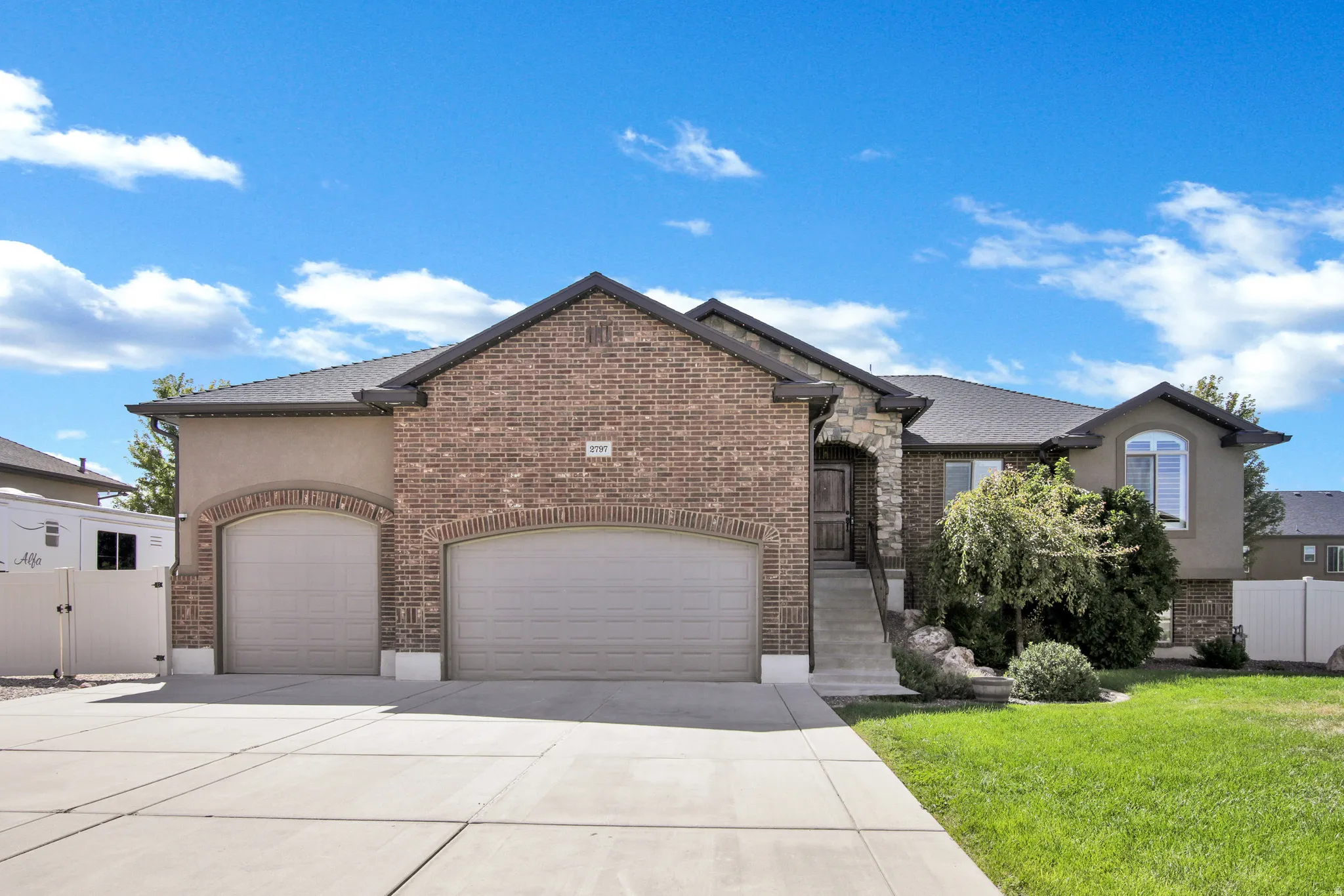 Brick and stucco exterior with stone accents, featuring a two-car garage with arched doorways, a concrete driveway, and a landscaped front yard