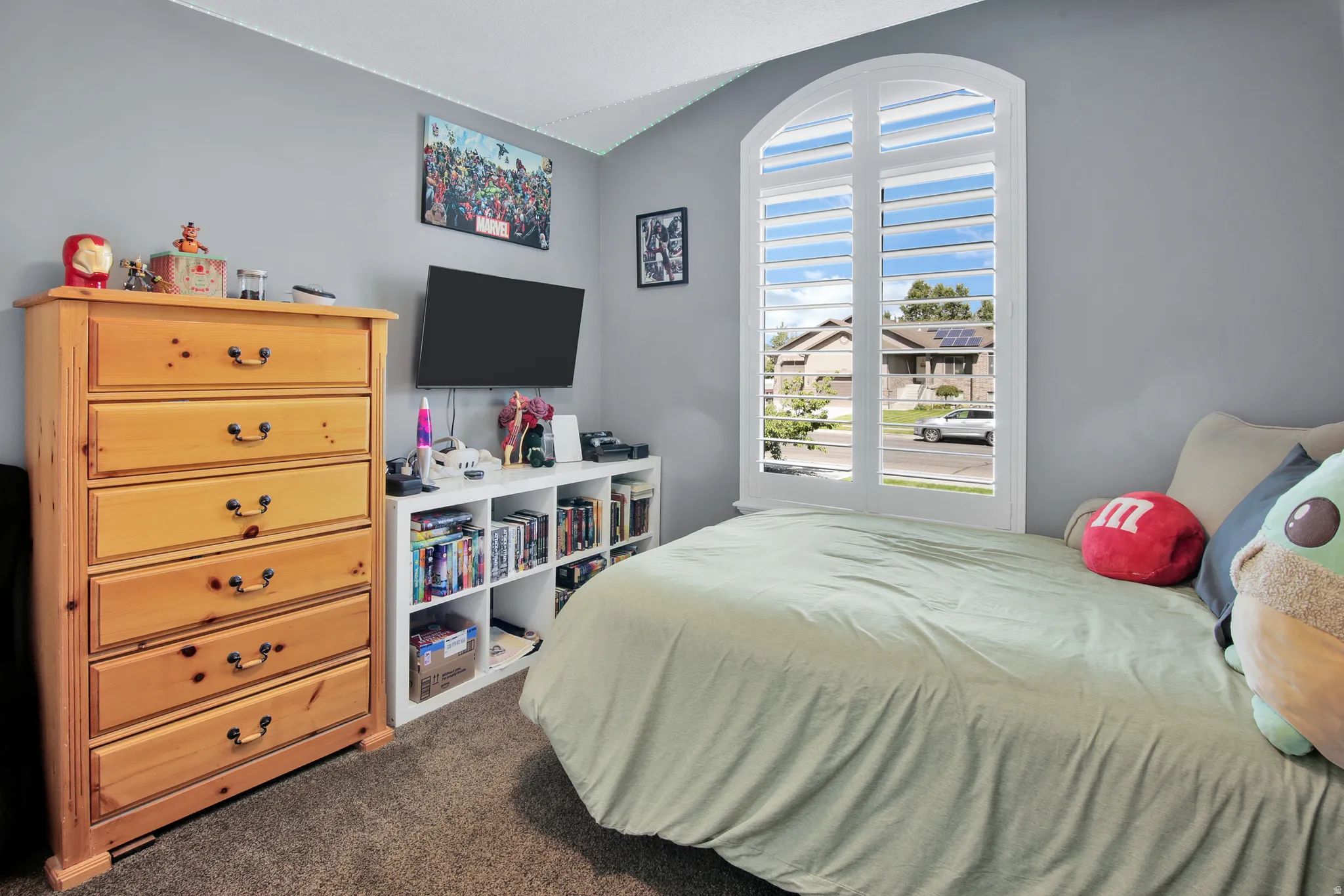 Arched window with plantation shutters, wall-mounted television, and built-in shelving