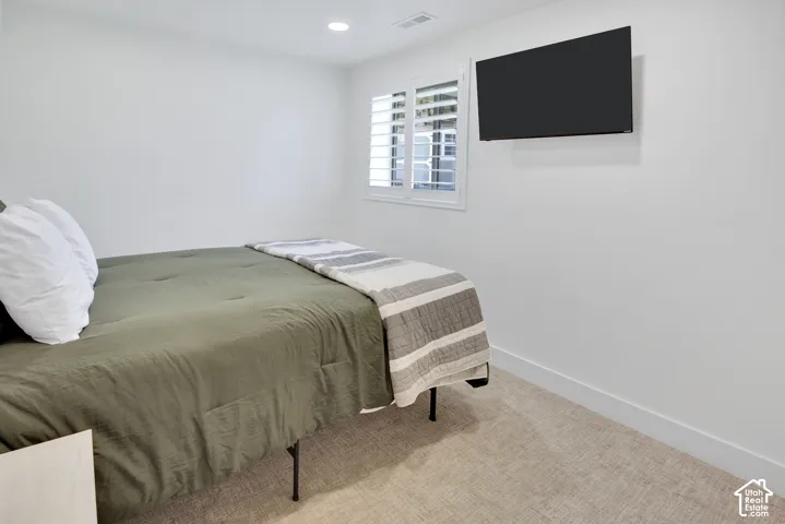 Recessed lighting, wall-mounted television, window with plantation shutters, light-toned carpeting, and white walls