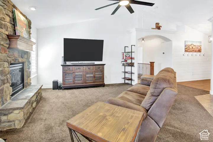 Vaulted ceilings, stone-clad fireplace with mantel, ceiling fan, and carpeted flooring
