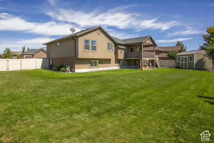 Expansive green lawn with a privacy fence, two-story exterior with stucco and brick accents, elevated deck with staircase, and an accessory storage shed