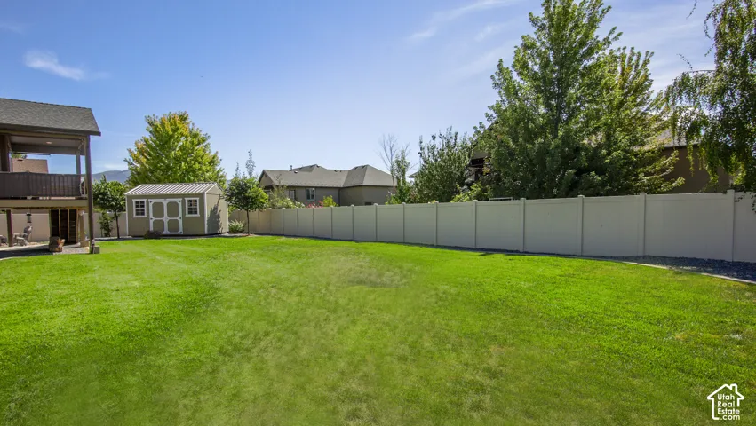Expansive green lawn with a privacy fence, a detached storage shed, and mature trees