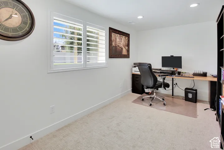 Recessed lighting illuminates the room, featuring a window with plantation shutters and carpeting