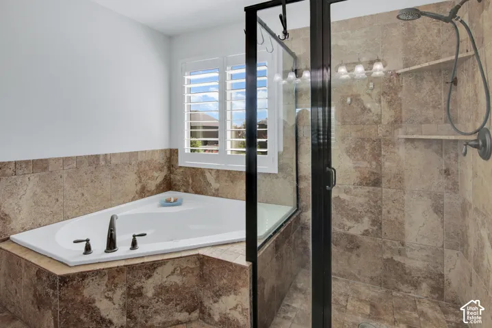 Corner soaking tub with bronze-finish fixtures, tile surround, and plantation shutters