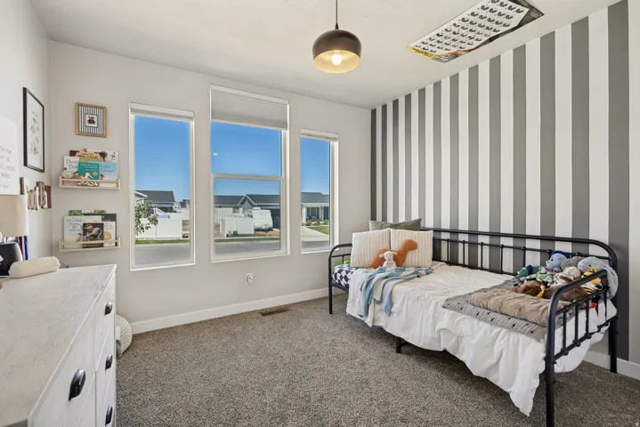 Plush carpet flooring, a decorative accent wall, multiple windows, and a ceiling-mounted light fixture